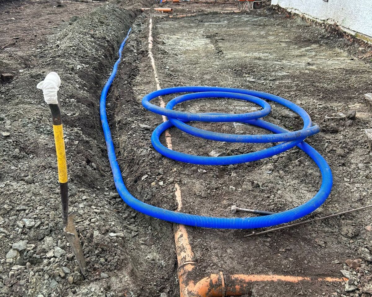 Blue hose coiled on a dirt construction site with a pipe and tools in the background.