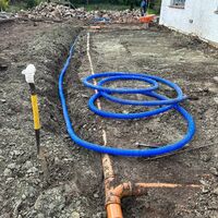 Blue hose coiled on a dirt construction site with a pipe and tools in the background.
