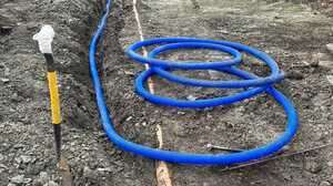 Blue perforated land drain coiled in an open trench across excavated ground beside a house