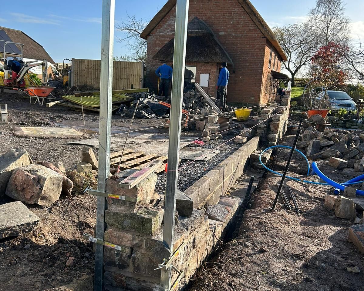 Construction site with a stone foundation being built, surrounded by tools and materials.