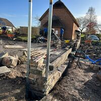 Construction site with a stone foundation being built, surrounded by tools and materials.