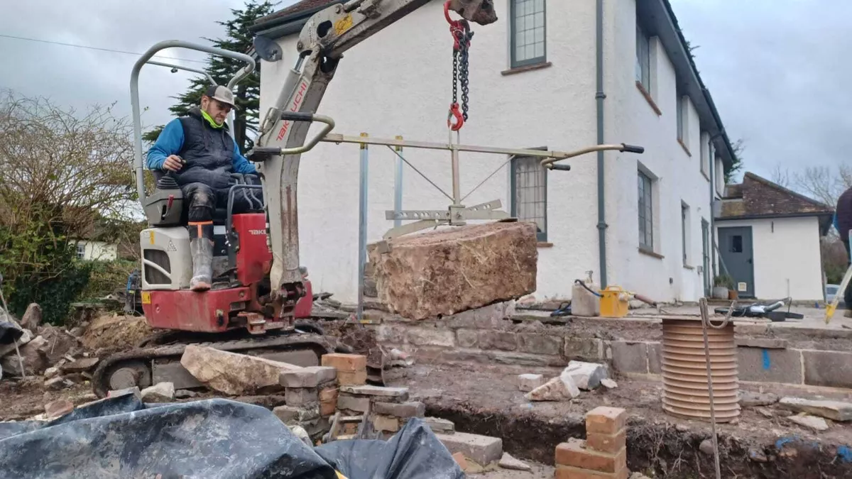 Excavator lifting reclaimed stone during groundworks for a garden transformation in Somerset