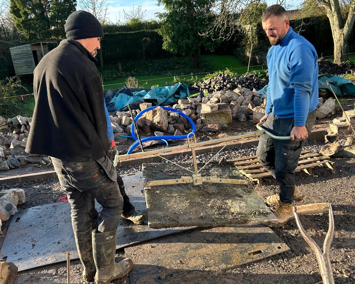Two men working outdoors on a construction site with tools and materials around them.