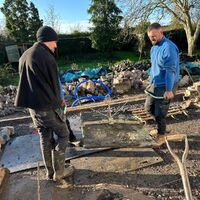 Two men working outdoors on a construction site with tools and materials around them.