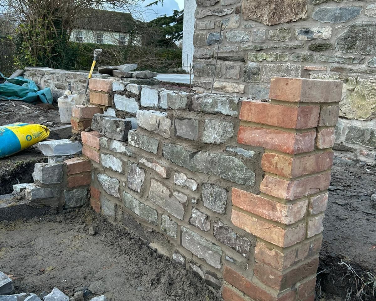Partially built stone wall with brick corners, surrounded by construction materials.