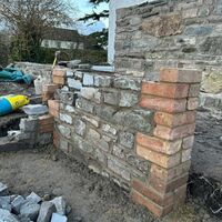 Partially built stone wall with brick corners, surrounded by construction materials.