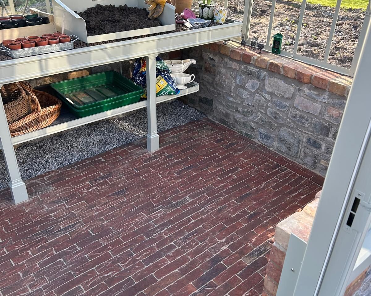 Interior of a greenhouse with a brick floor and shelves for planting tools and soil.