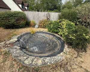Old circular pond with an empty liner and dry lawn before the new pond was built