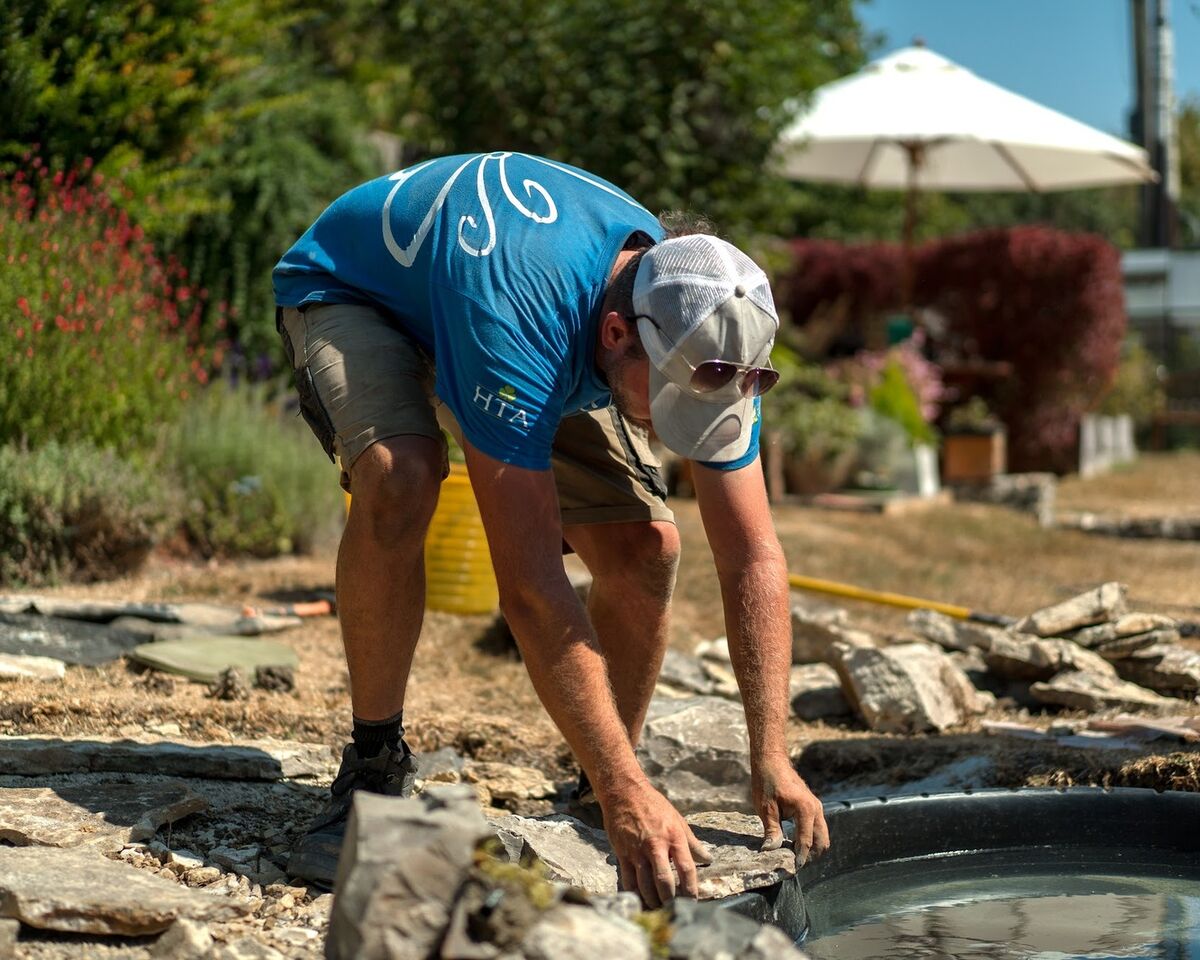 Team member placing rocks along the pond edge on a sunny day