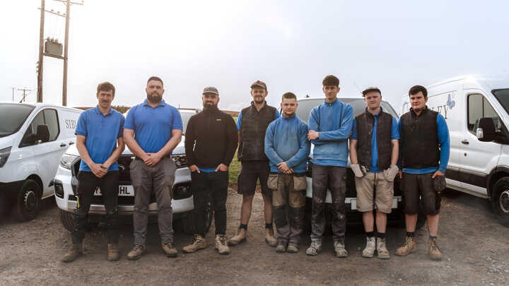 Garden with raised planter beds, green grass, and trees under a cloudy sky.